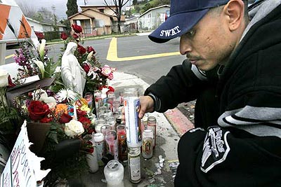 At a street shrine Sunday, Maurico Solano lights a candle for his friend, Marcos Salas, shot to death across from Aragon Avenue Elementary School.