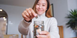 A person smiling and dropping coins into a jar