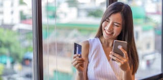 Woman smiling holding an Amex Blue Cash Preferred card and a mobile phone