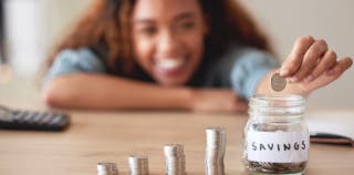 A woman smiling and dropping a coin into a savings jar