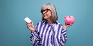 A woman holding a credit card and a piggy bank