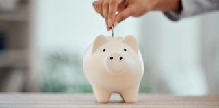 A hand dropping money in a piggy bank for savings