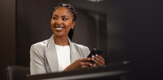 A smiling woman accessing her business checking account on a cell phone.