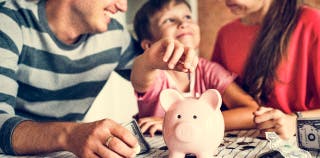 A child with their parents dropping a coin into a piggy bank for savings