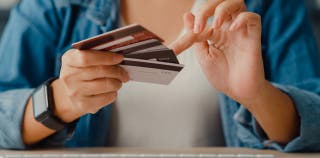 A woman holding three credit cards fanned out in front of her, pointing to one of them.