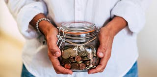 A person holding a jar full of coins for their savings account
