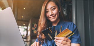 A person smiling and holding three credit cards in their hand.