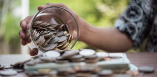 A person pouring out a jar of coins onto a table
