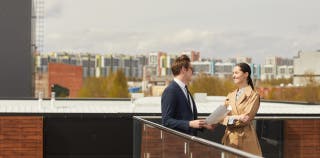 2 business people discuss work on a rooftop terrace overlooking a city