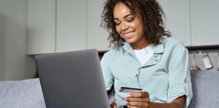A woman sitting in front of a computer, smiling, while holding an Capital One Venture credit card