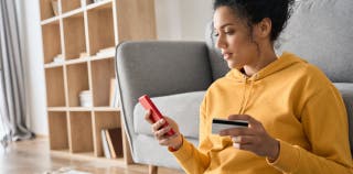 A woman in her living room with her phone in one had and her Capital One card in the other.