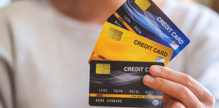 A person is holding a blue, a yellow, and a black credit card fanned out in their hand.
