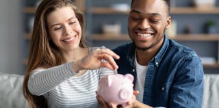 A couple smiling and putting a coin into a piggy bank for savings