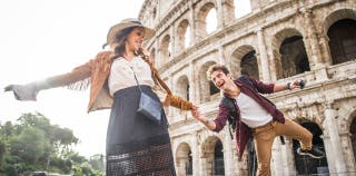 A man and woman holding hands in front of a stone colosseum.
