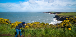 A person taking a picture with a camera on a tripod overlooking the cliffs in Ireland.