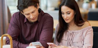 A man and woman looking at their joint checking accounts on their phones. 