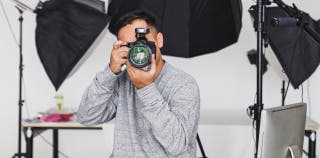 A man is holding a camera in front of his face with photography studio equipment behind him