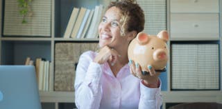 A woman smiling and holding a piggy bank.