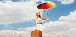 A woman holding a suitcase in one hand and an umbrella in the other with a background of a blue sky with clouds.