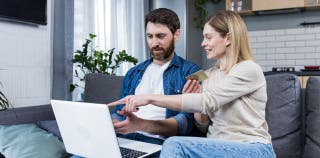 Man and woman looking and pointing at a laptop, discussing their credit utilization