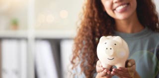 A woman smiling and holding a piggy bank.