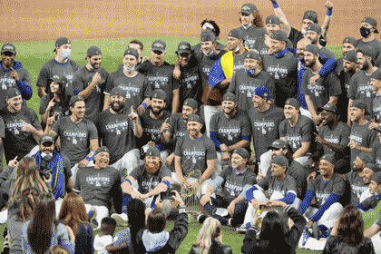Justin Turner's unmasked face amongst a group of Dodgers posing with their World Series trophy