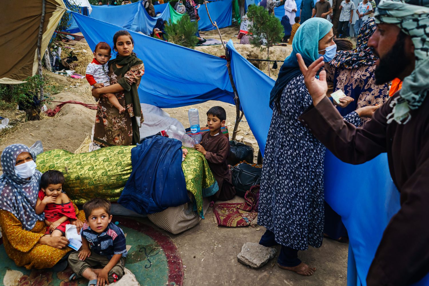 A man speaks with a group of women and children sitting outdoors.