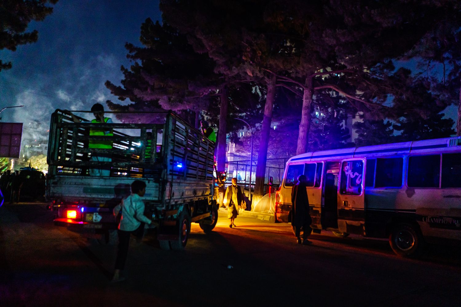 A street at night with cars lit up by colorful lights.