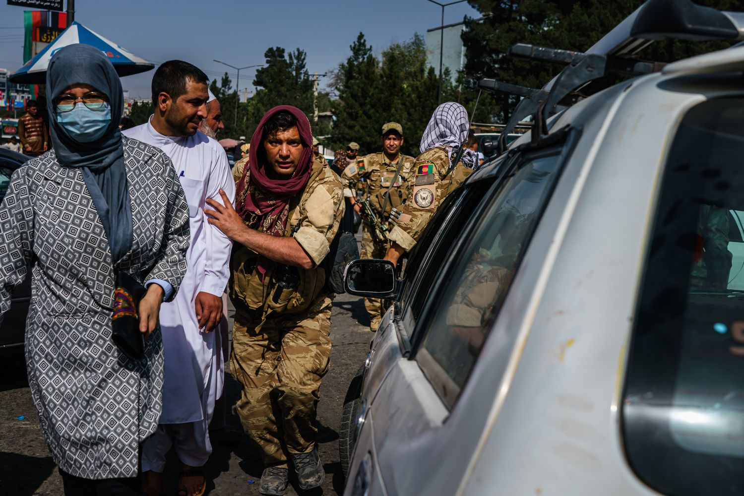 A Taliban fighter and pedestrians walk in a street filled with traffic.