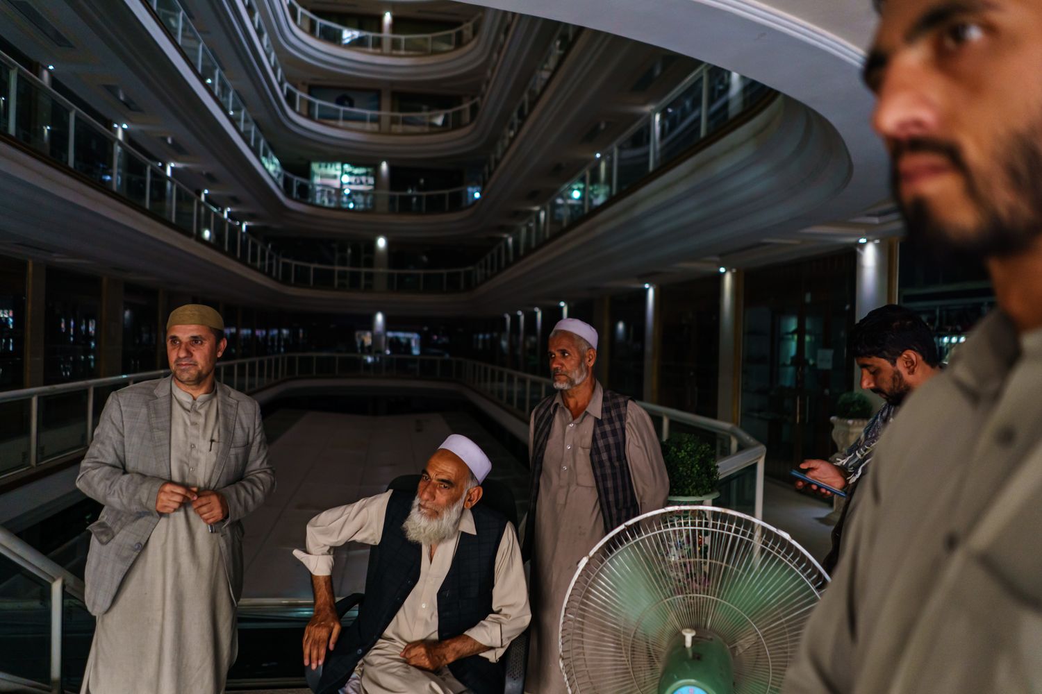 A group of men seated or standing inside a shopping mall.