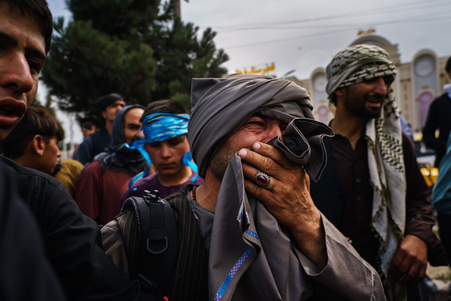A man covering his mouth weeping amongst a crowd gathered outside.