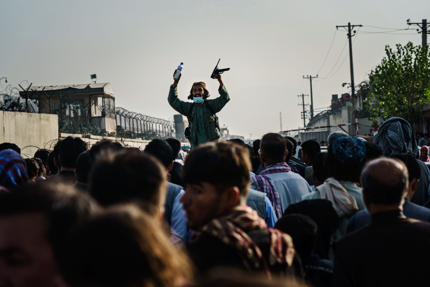 A Taliban fighter rises above a crowd of Afghans to stop them in a street.