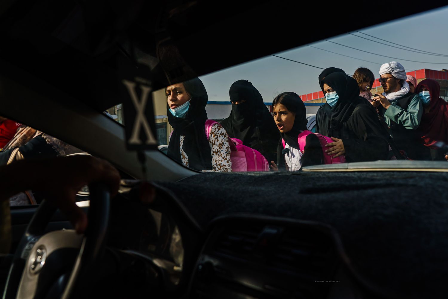 Women and girls with pink backpacks on are seen through a window from inside a car.