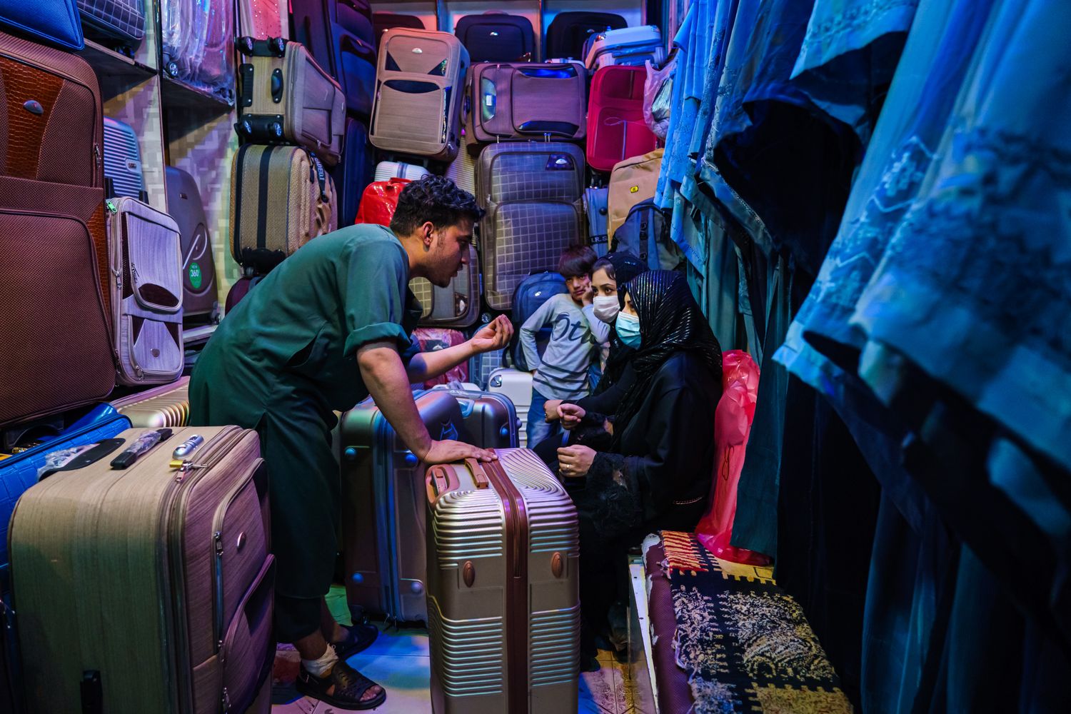 A man speaking with women and a child sitting inside a shop selling luggage.