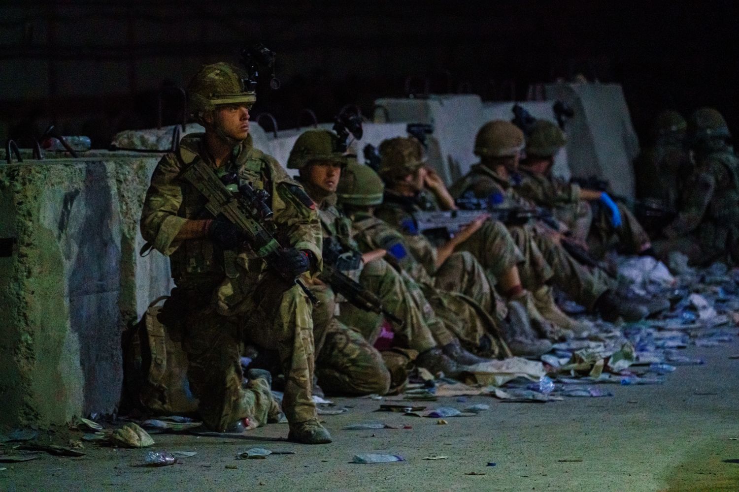 A group of soldiers sits along a wall at night.