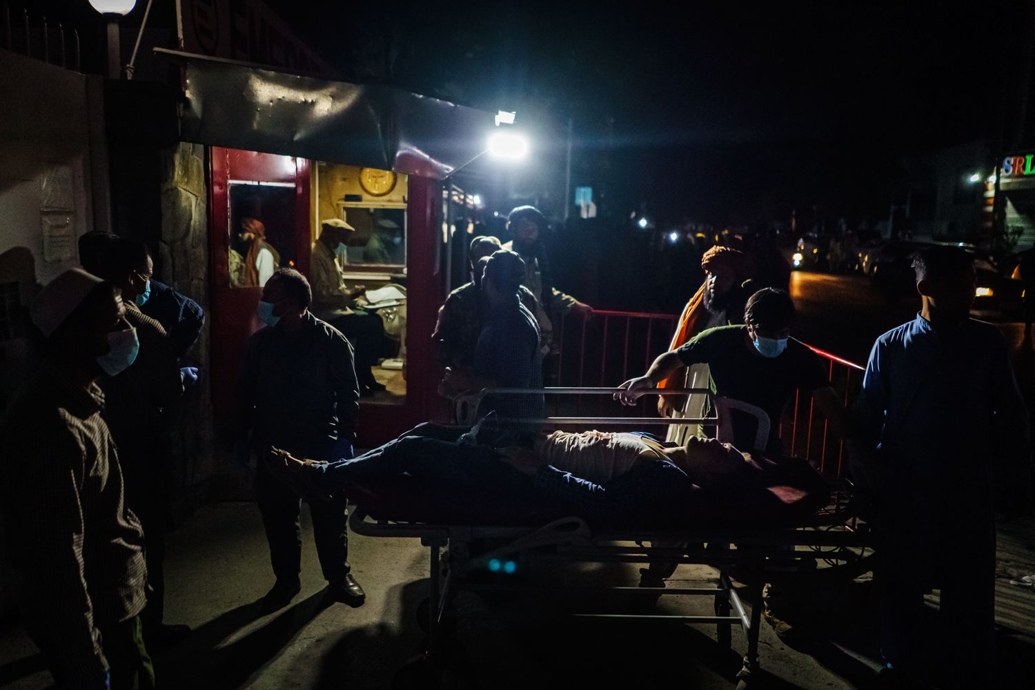 A wounded person on a stretcher is wheeled at night outdoors.