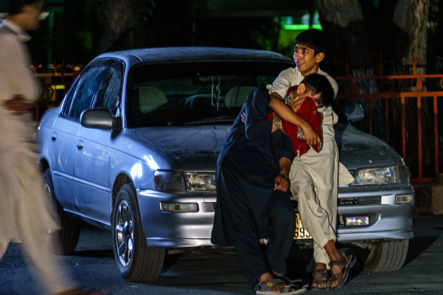 Two boys embrace each other as they weep in a parking lot of a hospital.