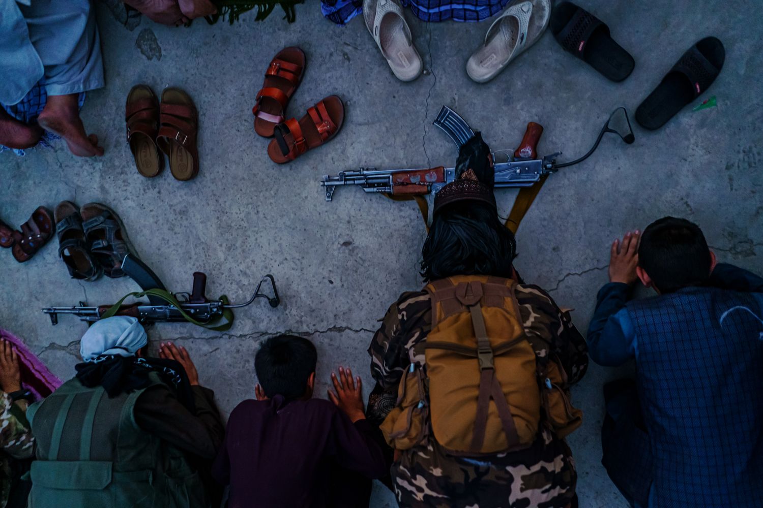 Taliban fighters kneel in prayers next to shoes and rifles.