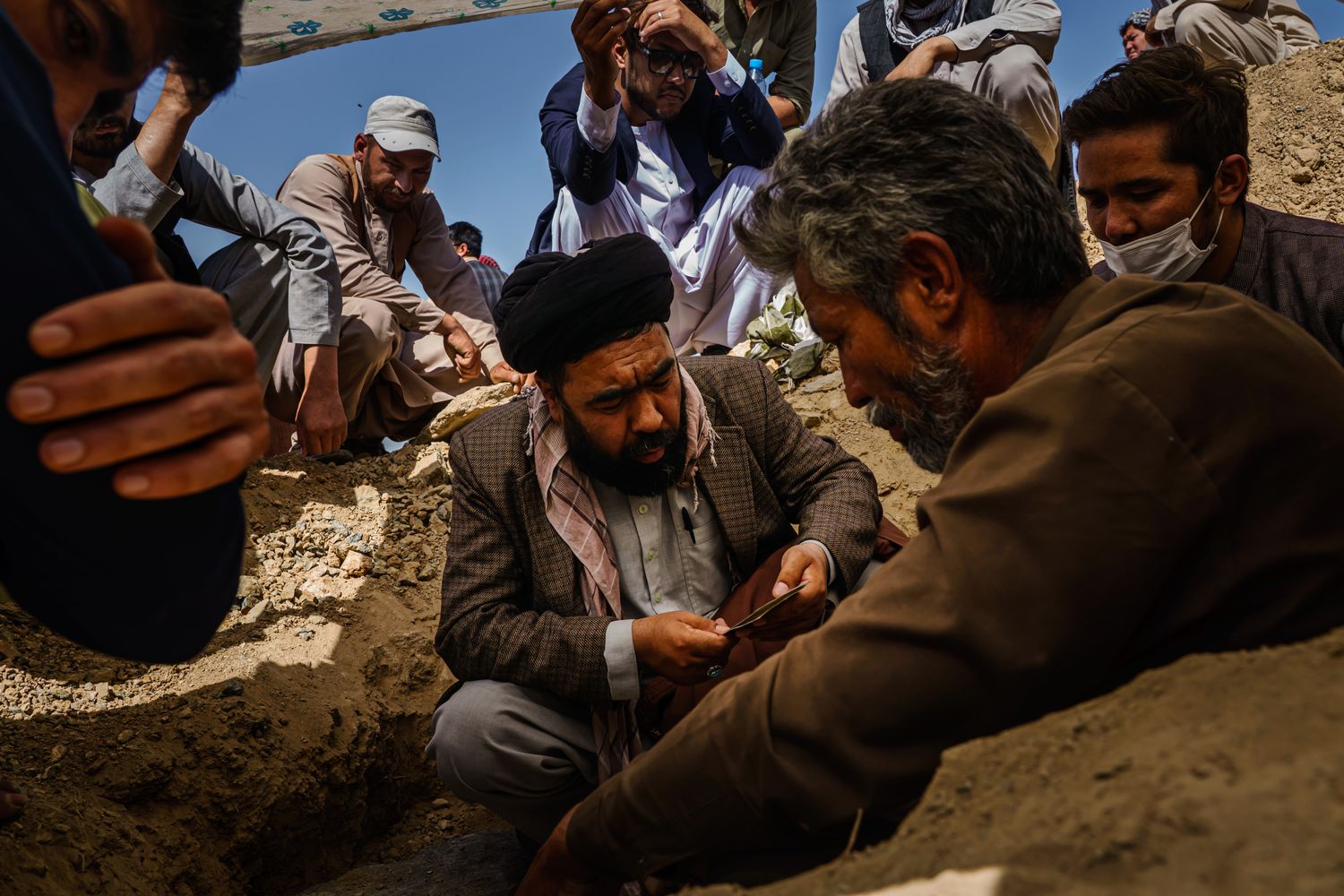 A man sitting in the middle of a group of men outdoors reads from a religious text.
