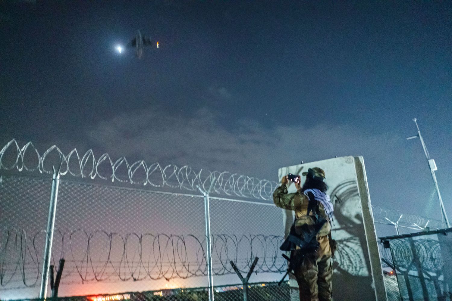 A Taliban fighter takes a photo of a plane in the sky with his mobile phone.
