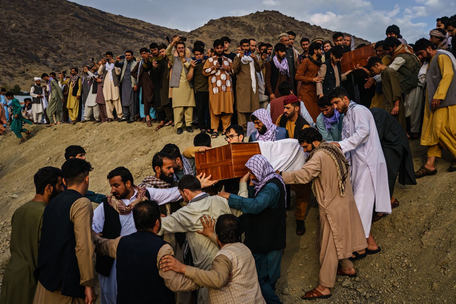A line of mourners follow a group of men carrying a coffin down a dirt embankment.