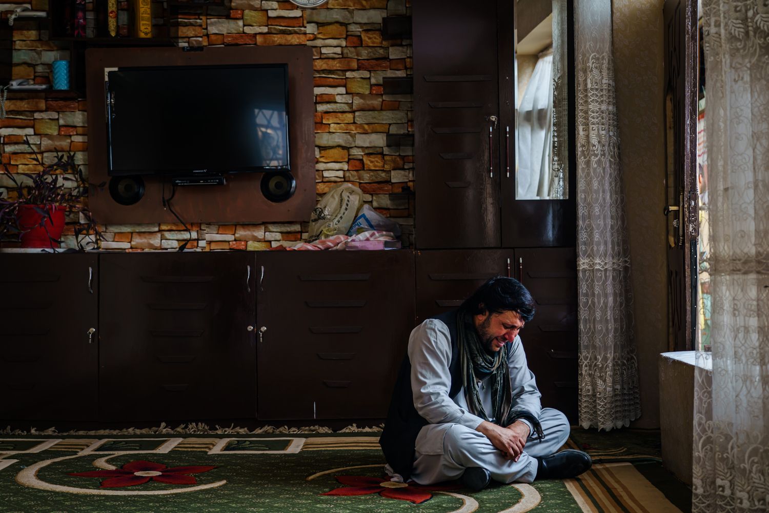 A man sits alone near a window weeping.
