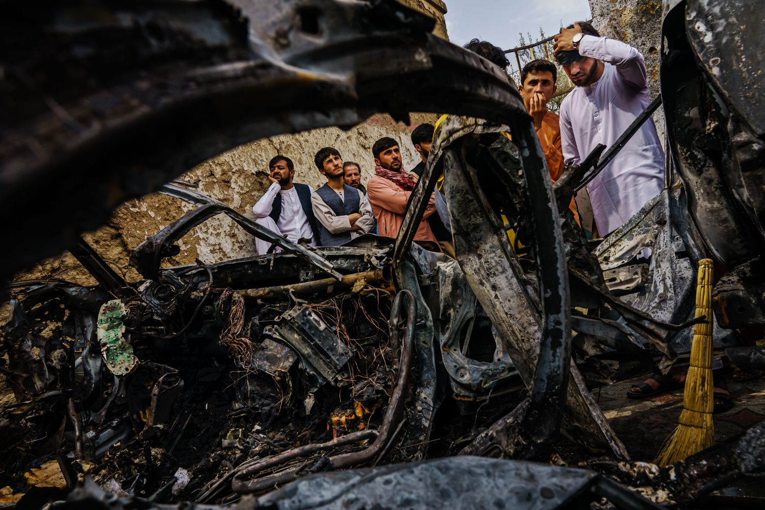 People gather near the charred ruins of a vehicle hit by a drone strike.