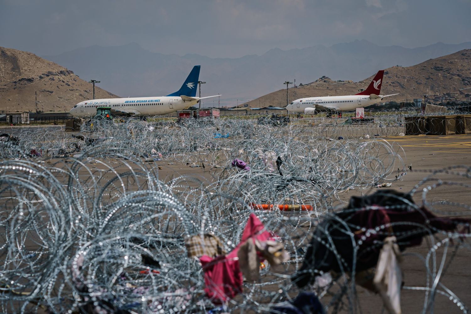 Two commercial planes are seen over a field of barbed wire.