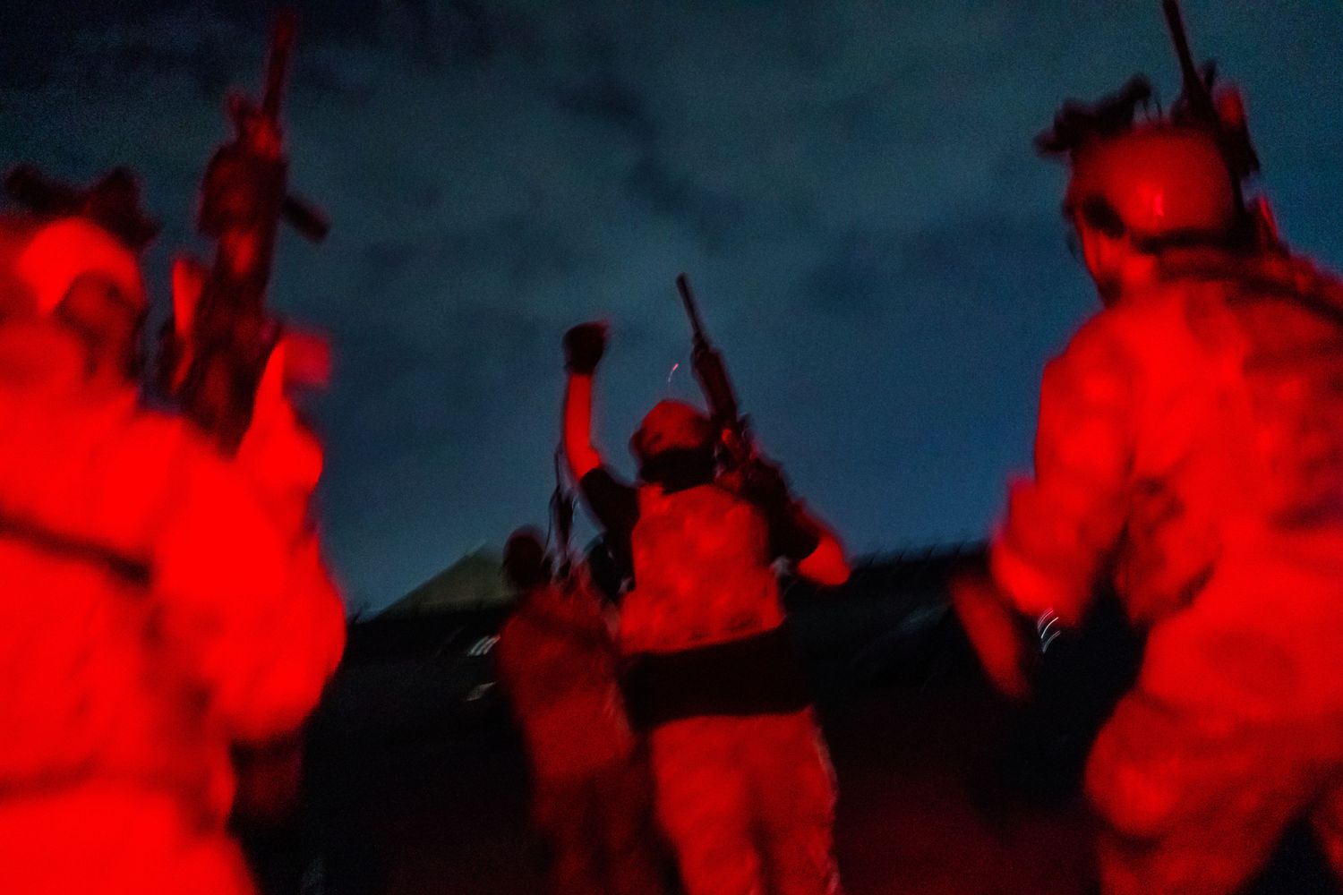 Taliban fighters aglow in red light run onto a tarmac at night.
