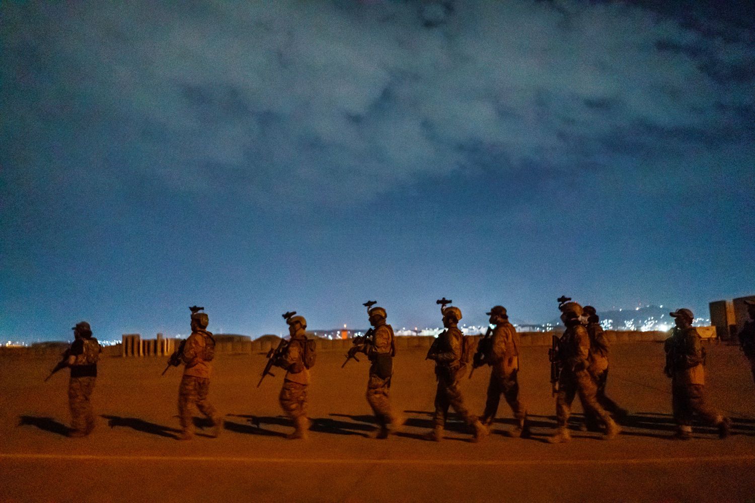 A procession of Taliban fighters walk on an airport tarmac at night.