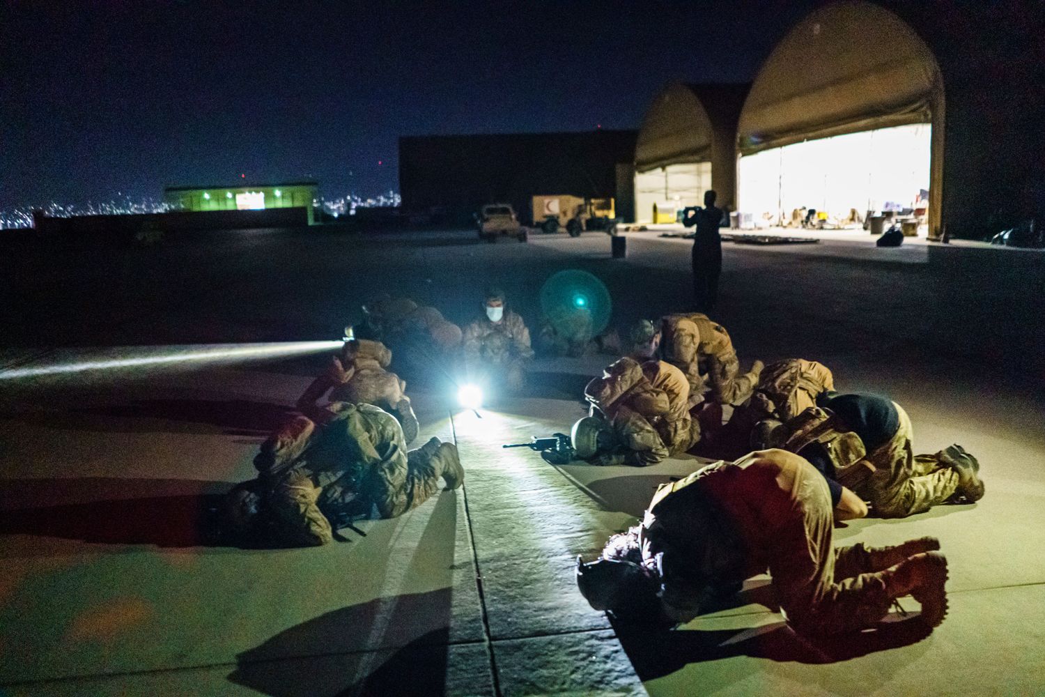 Taliban fighters kneel for evening prayers on an airport tarmac.