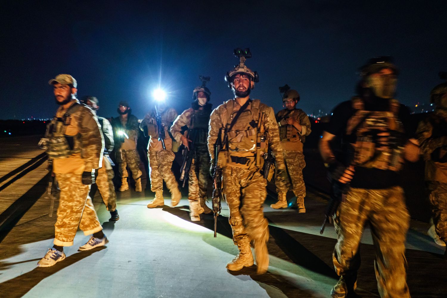 A group of Taliban fighters walks around an airport tarmac at night.