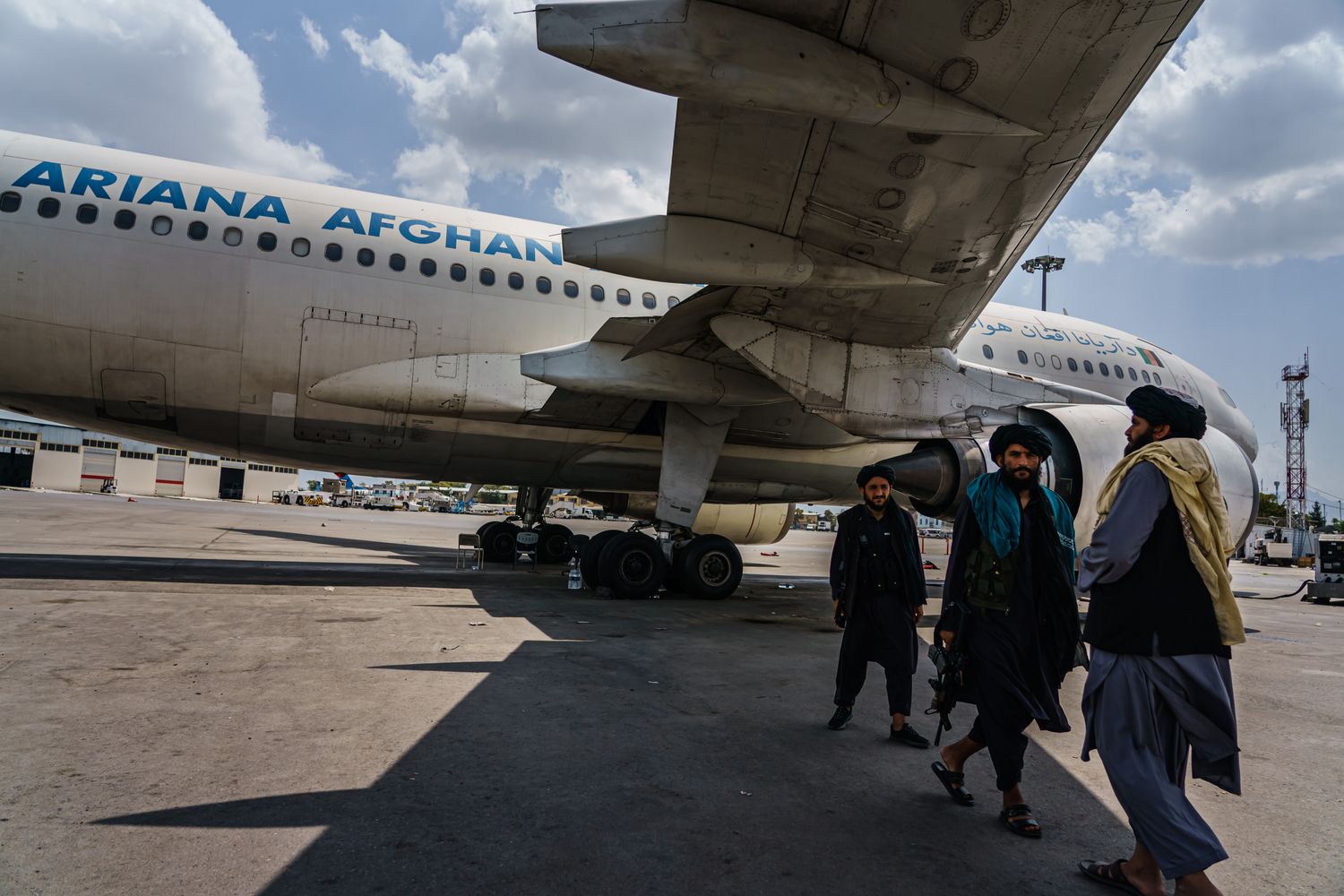Three men walk underneath the wing of a commercial plane.
