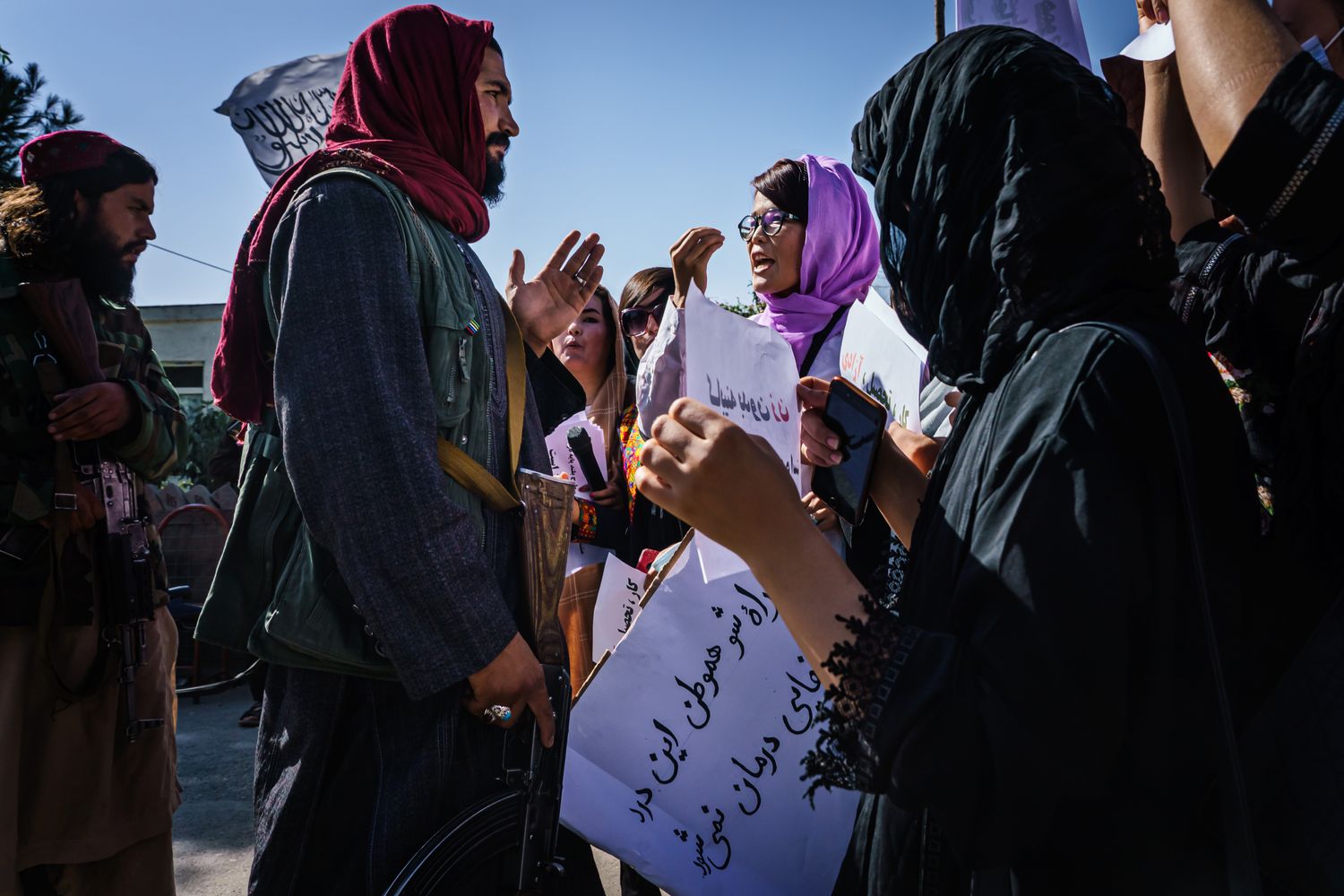 A Taliban fighter listens to a woman with a head scarf gesturing at him.